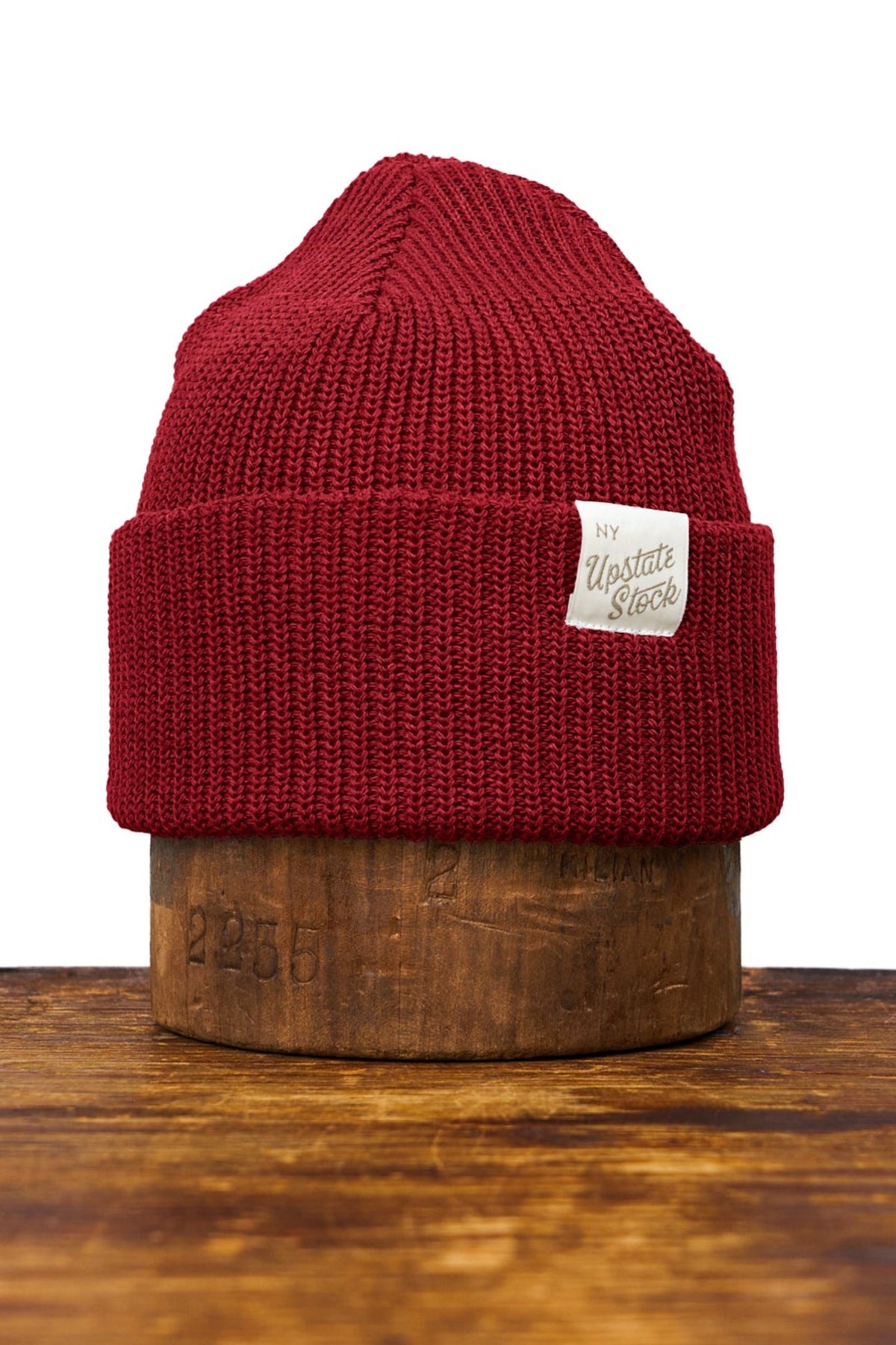 Red knit beanie with a brand label on a wooden block against a white background
