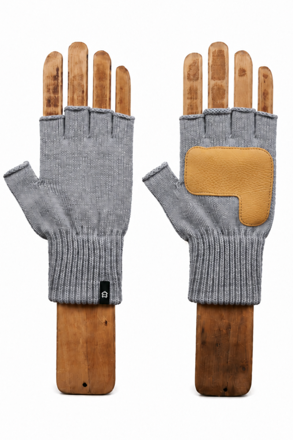 A pair of gray knit fingerless gloves displayed on wooden mannequin hands against a plain white background. One glove is shown from the palm side, revealing a tan leather patch on the back of the hand, and the other is shown from the back with the knit cuff.