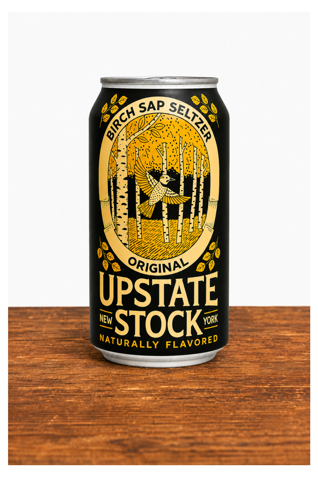 A 16 oz aluminum can of Upstate Stock New York Original Birch Sap Seltzer, featuring a black label with a gold illustration of a birch forest and a figure throwing a pumpkin, set on a wooden surface against a white background.